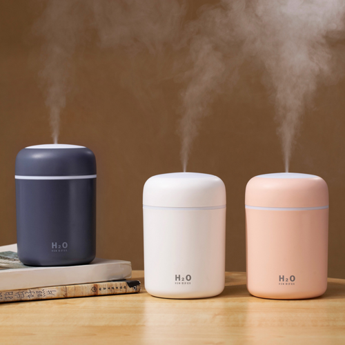 Three portable humidifiers with mist output in dark blue, white, and peach colors