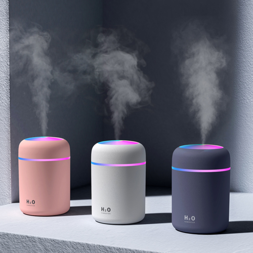 Three portable humidifiers with colored LED rings emitting mist in pink, white, and black