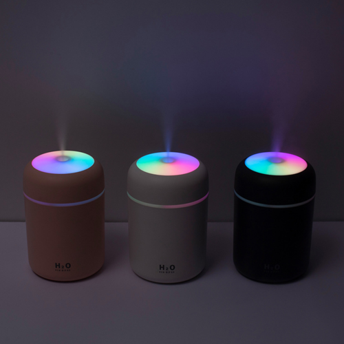 Three cylindrical portable humidifiers with glowing rainbow-colored tops in brown, gray, and black finishes